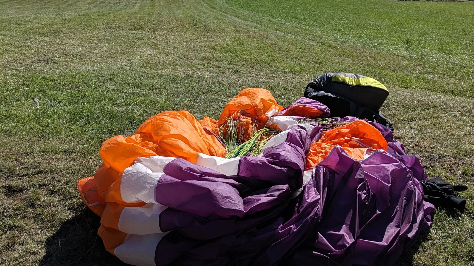 Une aile de parapente pliée dans l'herbe d'un décollage